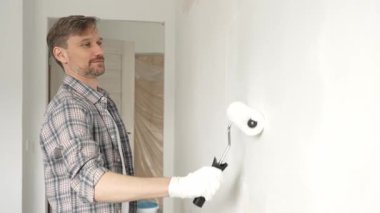 Profesyonel erkek ressam apartman duvarına beyaz boya sürüyor. Kapsamlı ev yenileme çalışmaları sırasında iç mekanı sürekli darbelerle değiştiriyor..