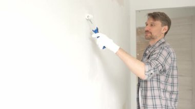 Profesyonel erkek ressam apartman duvarına beyaz boya sürüyor. Kapsamlı ev yenileme çalışmaları sırasında iç mekanı sürekli darbelerle değiştiriyor..