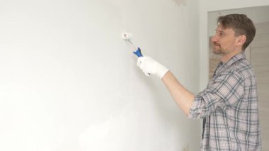 Orta yaşlı bir adam, apartman duvarında küçük bir silindirle beyaz boya yuvarlıyor. Geniş kapsamlı ev yenileme çalışmaları sırasında sürekli darbeler alarak iç mekanı değiştiriyor..