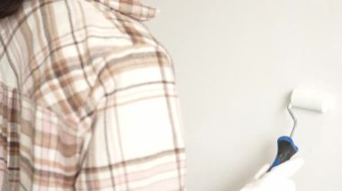 Eldivenli bir eli boya silindiri kullanarak kapamak, duvara yeni bir kat beyaz boya sürmek, bir ev yenileme projesi sırasında temiz ve eşit bir yüzey yaratmak