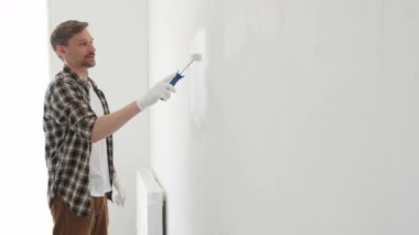 Profesyonel ressam beyaz duvarı silindirle düzleştiriyor, ev dekorasyonu sırasında koruyucu eldiven takıyor, iç mekanı yeni boyama tekniğiyle değiştiriyor.