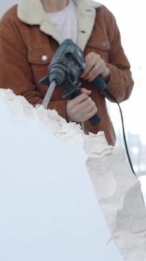 Tanımlanamayan inşaat işçisi beton duvarı döner çekiçle yıkıyor, koruyucu güvenlik teçhizatı takıyor, dikey görüntüyü kapatıyor. Yenileme konsepti.