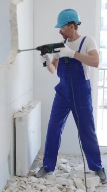 Güvenlik gözlüğü takan inşaat işçisi, bir duvarı yıkmak için döner çekiç matkabı kullanıyor, yenileme veya yenileme projesi sırasında enkaz ve toz yaratıyor.