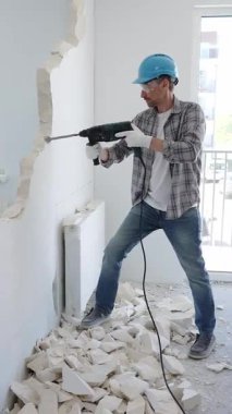 İnşaat işçisi, koruyucu teçhizatlı bir çekiç matkabıyla duvarı yıkıyor ve zemin yüzeyinde inşaat enkazı oluşturuyor. Yenileme konsepti.