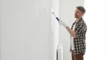 Profesyonel ressam beyaz duvarı silindirle düzleştiriyor, ev dekorasyonu sırasında koruyucu eldiven takıyor, iç mekanı yeni boyama tekniğiyle değiştiriyor.