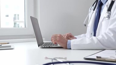 Doktor özenle bir dizüstü bilgisayarda yazıyor, muhtemelen hasta kayıtlarını güncelliyor veya araştırma yapıyor, modern bir tıbbi ortamda sağlık ve teknolojinin kesişimini gösteriyor.