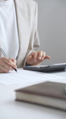 Professional accountant calculating annual tax, reviewing financial documents, tracking budget details at workplace desk with calculator and paperwork. Audit and taxes in business