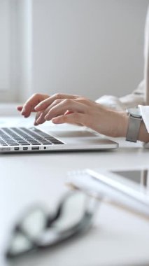 Şık bej bir takım elbise giymiş, gümüş bir saat takan, parlak beyaz bir masada oturan, dizüstü bilgisayara odaklanmış, işine odaklanmış bir iş kadını. İş adamları konsepti