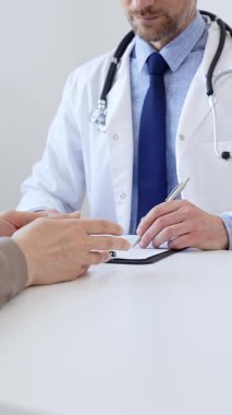 Doktor, klinikteki bir muayenede belirtilerini açıklayan bir kadın hastayı dinlerken not alıyor. İlaç ve sağlık hizmetleri kavramı.