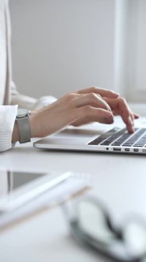 Şık bej bir takım elbise giymiş, gümüş bir saat takan, parlak beyaz bir masada oturan, dizüstü bilgisayara odaklanmış, işine odaklanmış bir iş kadını. İş adamları konsepti