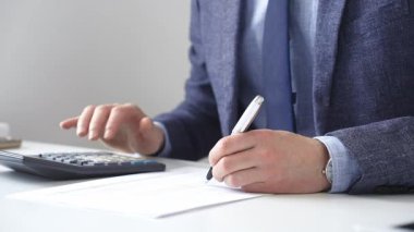 Hesap makinesi kullanan, not alan, hesaplamalar yapan ve ofis ortamında finansal verileri kaydeden bir iş adamı. Ticarette denetim ve vergiler