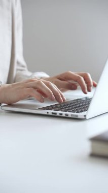 Şık bej bir takım elbise giymiş, gümüş bir saat takan, parlak beyaz bir masada oturan, dizüstü bilgisayara odaklanmış, işine odaklanmış bir iş kadını. İş adamları konsepti