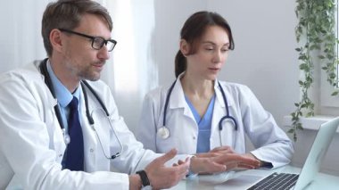 İki doktor bir dizüstü bilgisayardaki tıbbi kayıtları inceliyor, bir hastane veya klinik ortamdaki hasta verileri üzerine odaklanmış bir tartışmaya giriyorlar. İlaç ve sağlık hizmetleri kavramı.