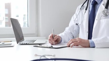 Erkek doktor reçete yazıyor ve bir ofis ortamındaki bir panoya tıbbi kayıtları dolduruyor. Sağlık ve hasta bakımının temel yönlerini gösteriyor. İlaç ve sağlık hizmetleri.