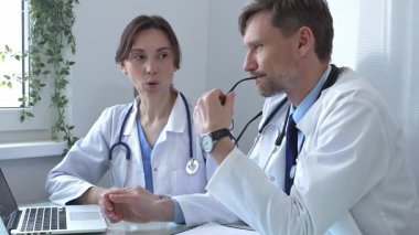 İki doktor bir dizüstü bilgisayardaki tıbbi kayıtları inceliyor, bir hastane veya klinik ortamdaki hasta verileri üzerine odaklanmış bir tartışmaya giriyorlar. İlaç ve sağlık hizmetleri kavramı.