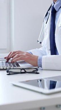 Doktor adam özenle bir dizüstü bilgisayarda yazıyor. Muhtemelen hasta kayıtlarını güncelliyor ya da araştırma yapıyor. Modern bir tıbbi ortamda sağlık ve teknolojinin kesişimini gösteriyor..