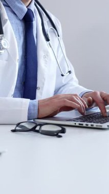 Doktor adam özenle bir dizüstü bilgisayarda yazıyor. Muhtemelen hasta kayıtlarını güncelliyor ya da araştırma yapıyor. Modern bir tıbbi ortamda sağlık ve teknolojinin kesişimini gösteriyor..