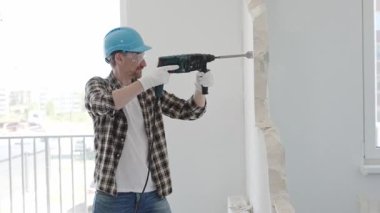 İnşaat işçisi, koruyucu teçhizatlı bir çekiç matkabıyla duvarı yıkıyor ve zemin yüzeyinde inşaat enkazı oluşturuyor. Yenileme konsepti.