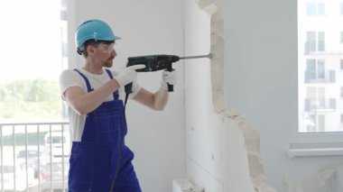 Güvenlik gözlüğü takan inşaat işçisi, bir duvarı yıkmak için döner çekiç matkabı kullanıyor, yenileme veya yenileme projesi sırasında enkaz ve toz yaratıyor.