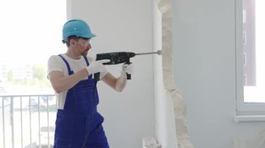 Güvenlik gözlüğü takan inşaat işçisi, bir duvarı yıkmak için döner çekiç matkabı kullanıyor, yenileme veya yenileme projesi sırasında enkaz ve toz yaratıyor.