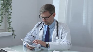 Laboratuvar önlüğü ve steteskop giyen tıp doktoru yanında dizüstü bilgisayarla parlak tıp ofisinde dijital tablet danışma hasta verileri kullanıyor. İlaç ve sağlık hizmetleri.