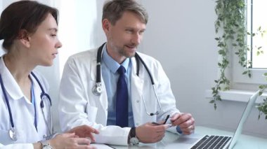 İki doktor bir dizüstü bilgisayardaki tıbbi kayıtları inceliyor, bir hastane veya klinik ortamdaki hasta verileri üzerine odaklanmış bir tartışmaya giriyorlar. İlaç ve sağlık hizmetleri kavramı.