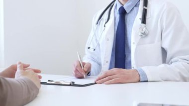 Doktor, klinikteki bir muayenede belirtilerini açıklayan bir kadın hastayı dinlerken not alıyor. İlaç ve sağlık hizmetleri kavramı.