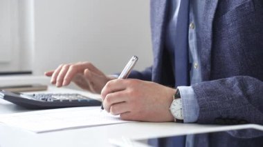 Hesap makinesi kullanan, not alan, hesaplamalar yapan ve ofis ortamında finansal verileri kaydeden bir iş adamı. Ticarette denetim ve vergiler
