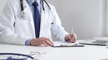 Erkek doktor reçete yazıyor ve bir ofis ortamındaki bir panoya tıbbi kayıtları dolduruyor. Sağlık ve hasta bakımının temel yönlerini gösteriyor. İlaç ve sağlık hizmetleri.