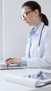 Kadın doktor, parlak bir tıp bürosundaki dizüstü bilgisayarında, sağlık teknolojisi ve tıbbi belgeler sergiliyor. İlaç ve sağlık hizmetleri kavramı.