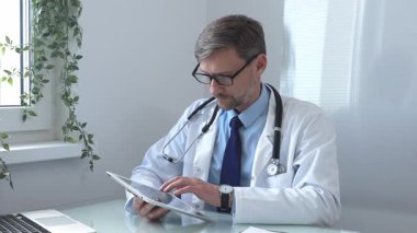 Laboratuvar önlüğü ve steteskop giyen tıp doktoru yanında dizüstü bilgisayarla parlak tıp ofisinde dijital tablet danışma hasta verileri kullanıyor. İlaç ve sağlık hizmetleri.