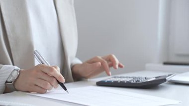 Yıllık vergisini hesaplayan profesyonel muhasebeci, mali belgeleri gözden geçiren, iş yerindeki bütçe detaylarını hesap makinesi ve evrak işleriyle takip eden. Ticarette denetim ve vergiler