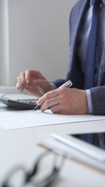 Hesap makinesi kullanan, not alan, hesaplamalar yapan ve ofis ortamında finansal verileri kaydeden bir iş adamı. Ticarette denetim ve vergiler