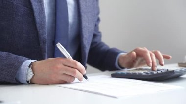 Hesap makinesi kullanan, not alan, hesaplamalar yapan ve ofis ortamında finansal verileri kaydeden bir iş adamı. Ticarette denetim ve vergiler