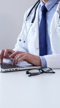 Doktor adam özenle bir dizüstü bilgisayarda yazıyor. Muhtemelen hasta kayıtlarını güncelliyor ya da araştırma yapıyor. Modern bir tıbbi ortamda sağlık ve teknolojinin kesişimini gösteriyor..