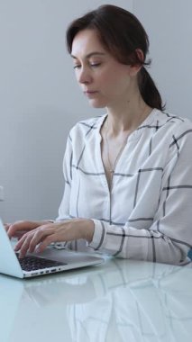 Gösterişli cam bir masada oturan odaklanmış iş kadını, parlak, modern bir ofiste dizüstü bilgisayarıyla yazı yazıyor, tamamen işine dalmış ve profesyonellik ve güven saçıyor. İş adamları konsepti