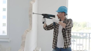 İnşaat işçisi, koruyucu teçhizatlı bir çekiç matkabıyla duvarı yıkıyor ve zemin yüzeyinde inşaat enkazı oluşturuyor. Yenileme konsepti.