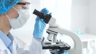 Araştırma örneğini mikroskop üzerinden inceleyen kadın bilim adamı tıbbi araştırma için koruyucu laboratuvar malzemesi giyiyor. Laboratuvar ve bilim konsepti.