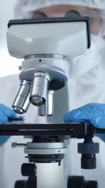 Tehlikeli madde giysisi, maskesi ve eldiveni olan bir tıp virologu bir laboratuvar araştırma virüsünün mikroskobunda özenle çalışıyor. Sağlık ve Bilim Konsepti.
