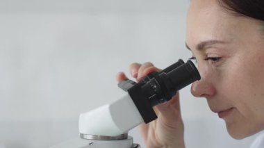Modern bir laboratuvarda araştırmalarını yürütürken mikroskopla inceleyen kadın bilim adamı çalışmalarına ve bilimsel keşiflerine odaklandı. Tıp ve bilim konsepti.