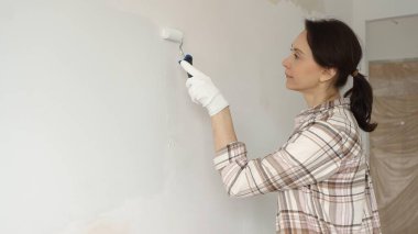 Profesyonel bir ressam koruyucu eldivenler giyerek duvarda pürüzsüz bir şekilde beyaz boya sürüyor, evin içini kusursuz bir fırça ve titiz bir boya tekniğiyle yeniliyor.