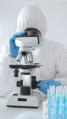 Koruyucu ekipman alanında çalışan bir tıp virologu laboratuvar ortamında araştırma yaparken mikroskop altında virüs örneklerini inceliyor..