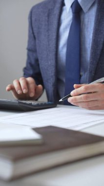 İş adamı hesap makinesi kullanıyor ve ofis ortamında finansal verileri kaydediyor. Ticarette denetim ve vergiler.