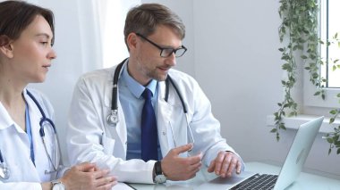 İki doktor bir dizüstü bilgisayarda tıbbi çizelgeleri inceliyor, hastane veya klinik ortamdaki hasta verilerini tartışıyorlar. Tıp ve sağlık hizmetleri kavramı