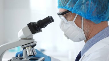 Koruyucu ekipman takan erkek bilim adamı mikroskop kaymasını inceliyor, steril laboratuvar ortamında araştırma örneklerini analiz ediyor, yakın plan. Tıp ve bilim konsepti.