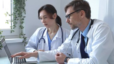 İki doktor bir dizüstü bilgisayarda tıbbi çizelgeleri inceliyor, hastane veya klinik ortamdaki hasta verilerini tartışıyorlar. Tıp ve sağlık hizmetleri kavramı