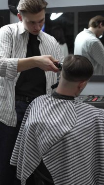 Profesyonel berber müşterilerin saçlarını elektrikli makasla dikkatlice buduyor, modern bir berber dükkanında şık ve kusursuz bir saç kesimi sağlıyor..