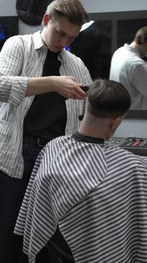 Profesyonel berber müşterilerin saçlarını elektrikli makasla dikkatlice buduyor, modern bir berber dükkanında şık ve kusursuz bir saç kesimi sağlıyor..