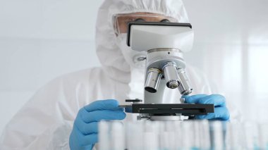 Koruyucu ekipman takan bilim araştırmacısı mikroskobu ayarlıyor, laboratuvar örneklerini steril araştırma ortamında hassasiyetle analiz ediyor. Tıp, sağlık ve bilim konsepti.