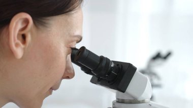 Modern bir laboratuvarda araştırmalarını yürütürken mikroskopla inceleyen kadın bilim adamı çalışmalarına ve bilimsel keşiflerine odaklandı. Tıp ve bilim konsepti.